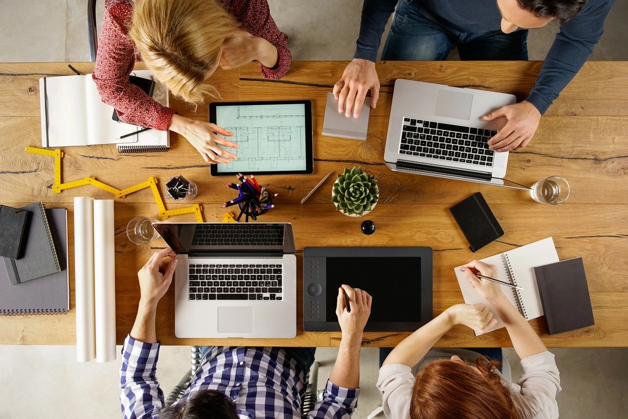 showing real estate transaction coordinators sitting around a desk with their computers and paperwork